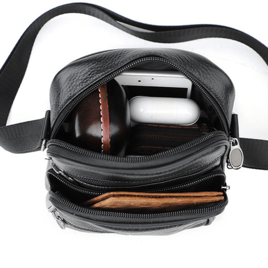 Interior view of a leather cross body bag showing multiple compartments and stored items like phone and wallet.