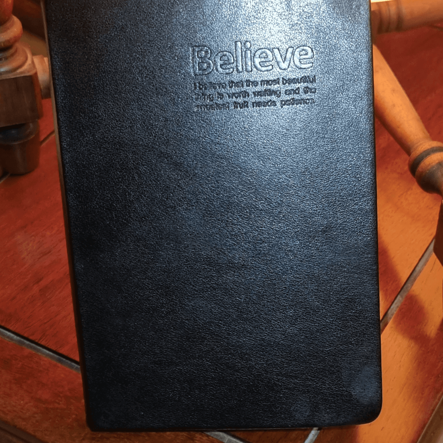 Black genuine leather travel journal with embossed 'Believe' quote on the cover, designed for luxurious writing.