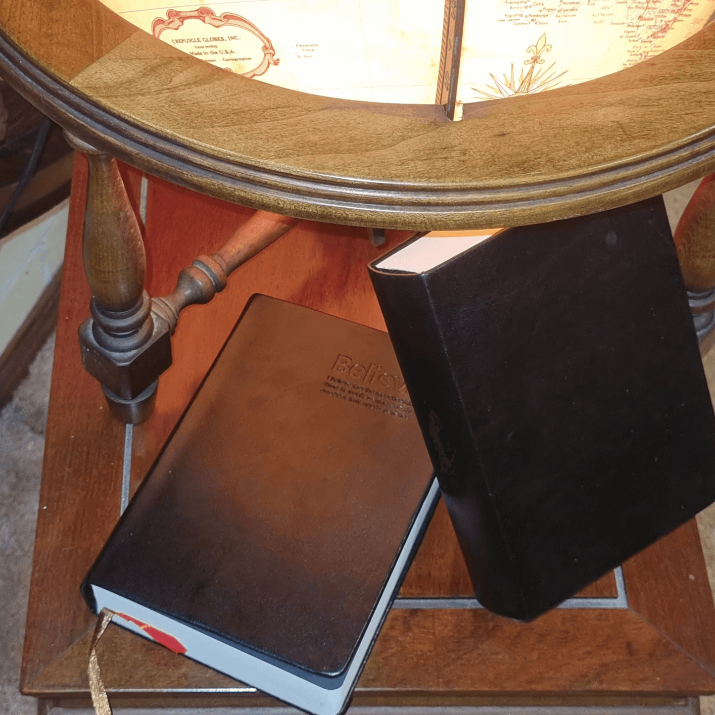Black Genuine Leather Travel Journal and a notebook beside a wooden globe on a table.