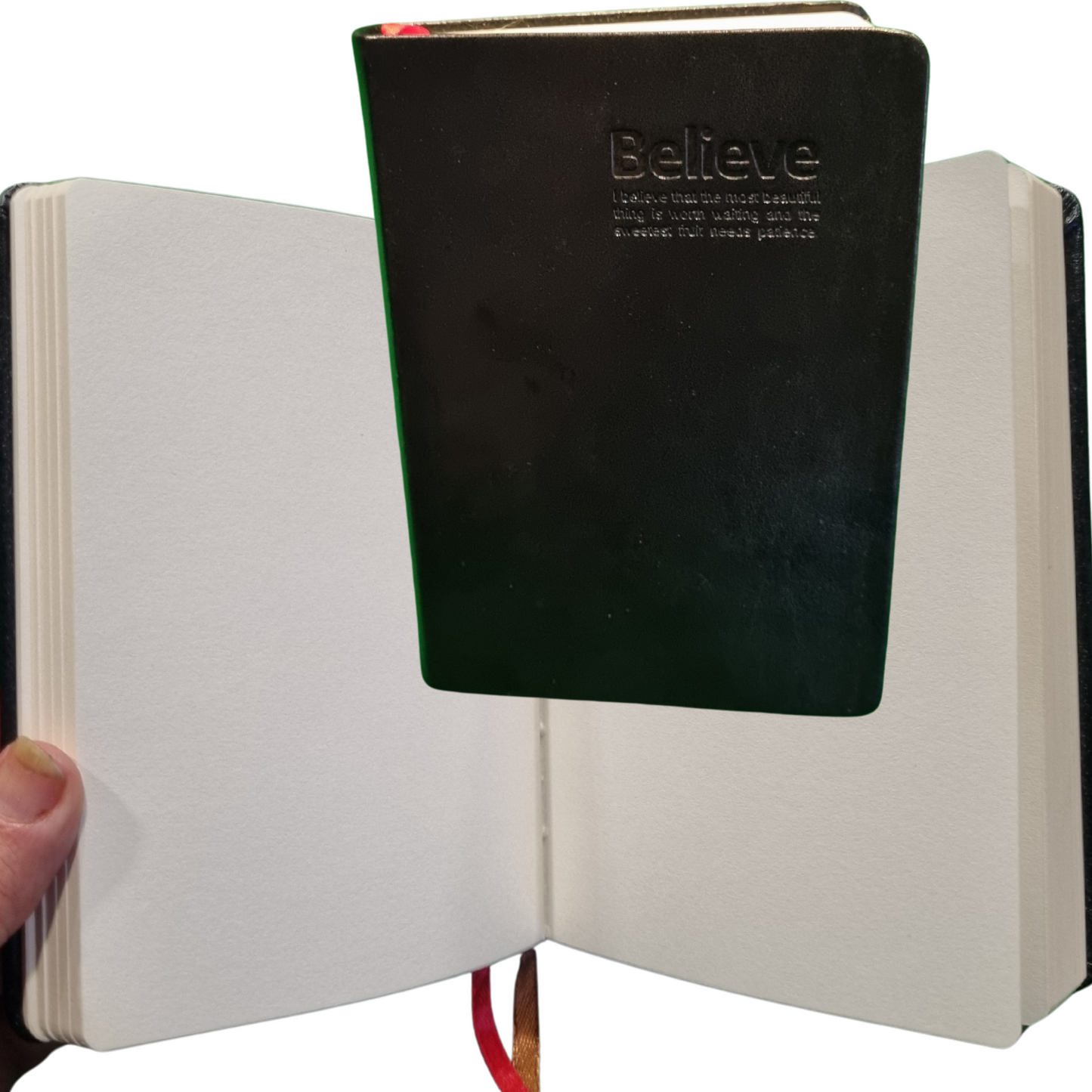 Black genuine leather travel journal with embossed 'Believe' and 240 blank pages open for writing.