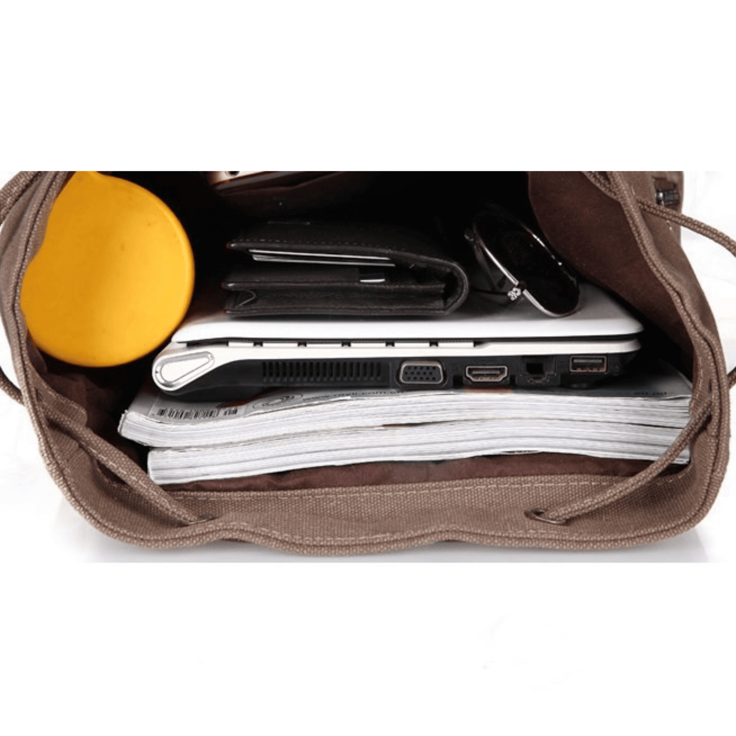 Interior view of a spacious canvas backpack filled with a laptop, notebooks, and a yellow coffee cup.