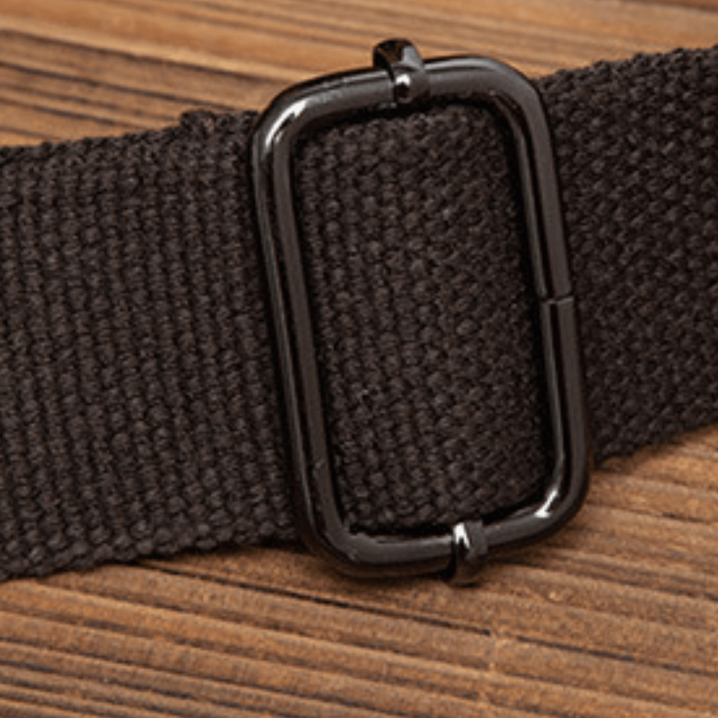 Close-up of a black strap with a metal buckle on wooden surface, showcasing quality craftsmanship.