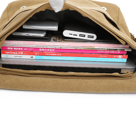 Inside view of a canvas messenger bag displaying a laptop, magazines, and a power bank, showcasing its spacious compartments.