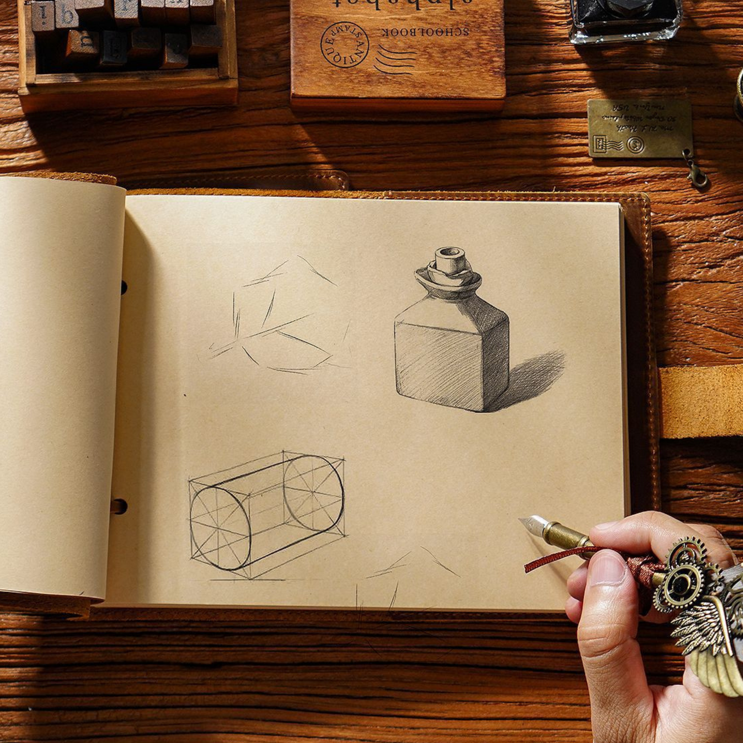 Sketches of a bottle and cylinder in a Crazy Horse leather bound sketchbook on a wooden table.